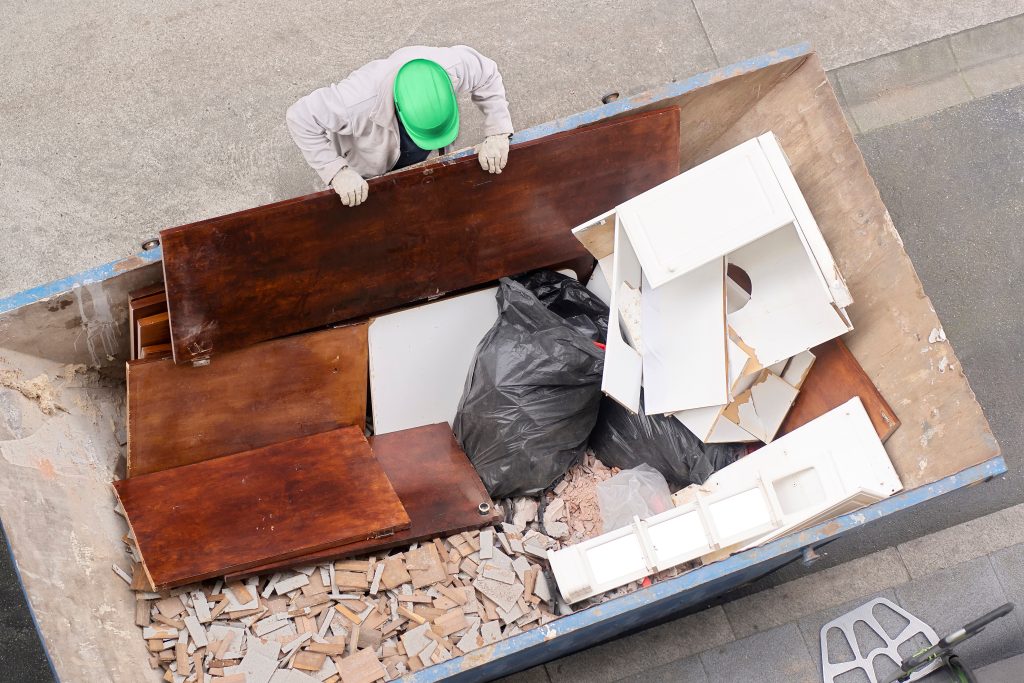 bricklayer depositing furniture and tiles in midi skip in street